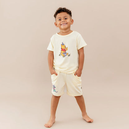 Young smiling boy wearing the Toddler Basic Tee in Winnie the Pooh on Chamomile paired with the Winnie the Pooh drawstring shorts on chamomile