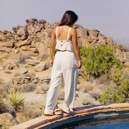 Woman wearing Tori Linen Tank in almond milk facing away, standing by pool with desert rocks in background