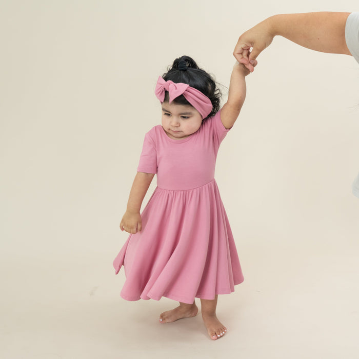 Young girl twirling wearing the Twirl Dress in Apple Blossom and matching knotted bow headband