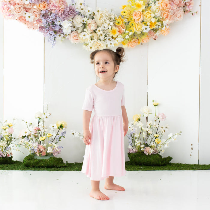 Child wearing Kyte Baby Short Sleeve Twirl Dress with ballerina neckline in Sakura