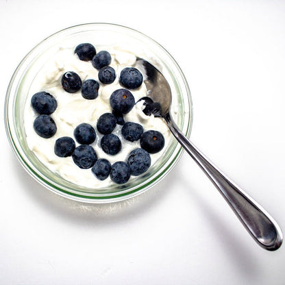 Glass bowl with yogurt and blueberries on a white background