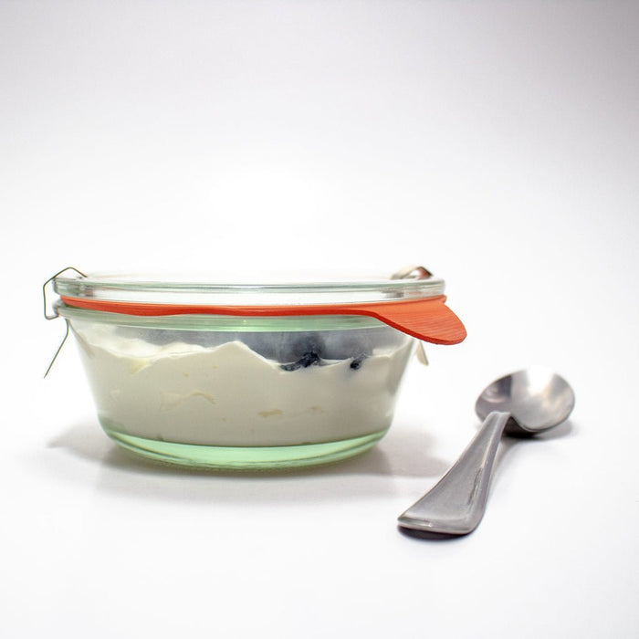 Glass food storage container with orange gasket and metal spoon on a white background