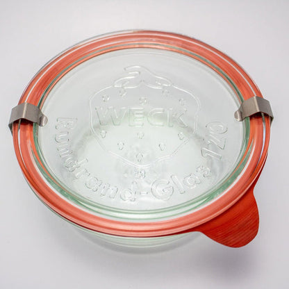 Clear glass Weck jar with an orange lid on a white background