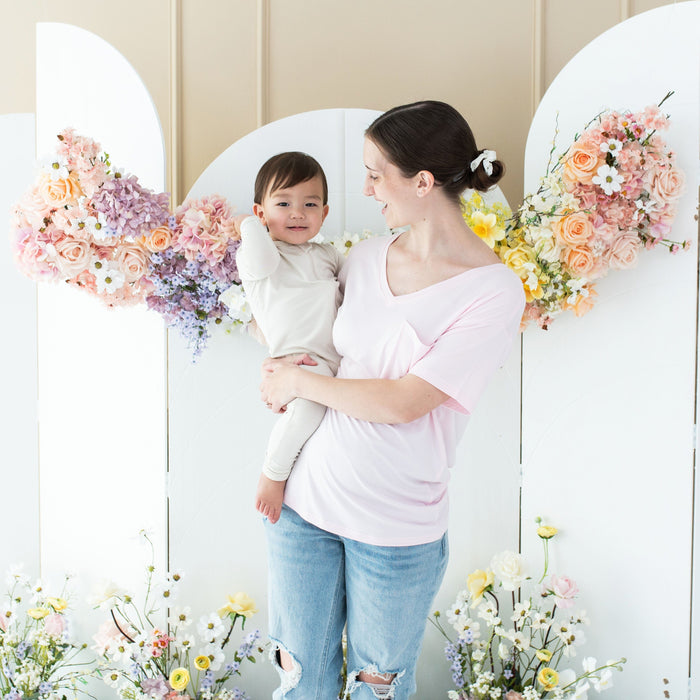 Woman wearing Kyte Baby Women's Relaxed Fit V-Neck tee in Sakura pink holding toddler