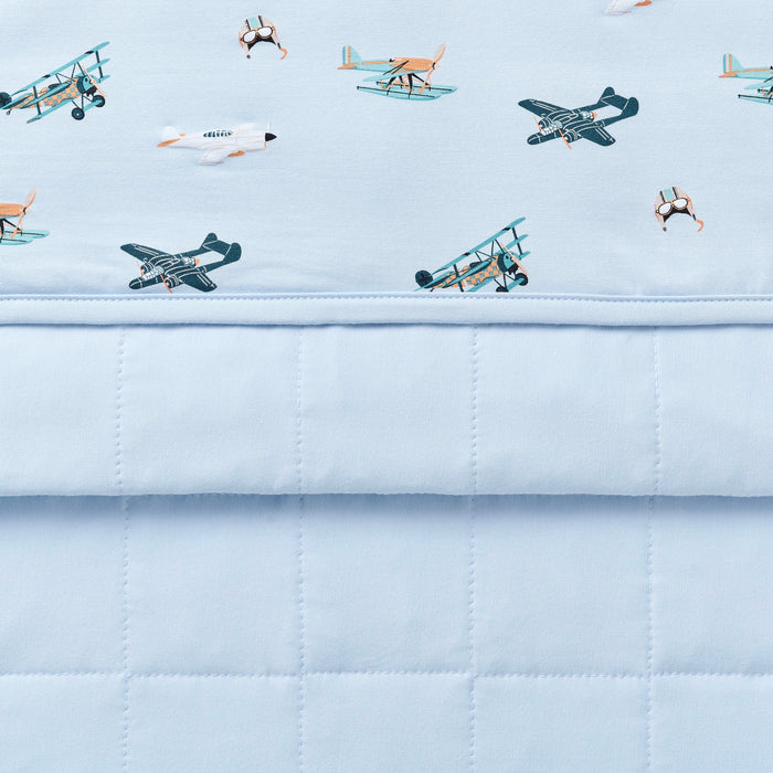 Close up of the Youth Blanket in Take Off 1.0 showing the baby blue quilted backing and plane print smooth top layer