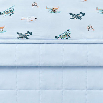 Close up of the Youth Blanket in Take Off 1.0 showing the baby blue quilted backing and plane print smooth top layer